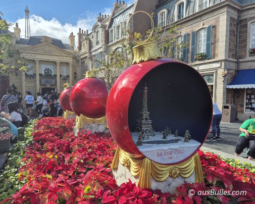 The French Pavilion at Disney's EPCOT park is adorned with giant Christmas ornaments featuring a Parisian neighborhood scene inside