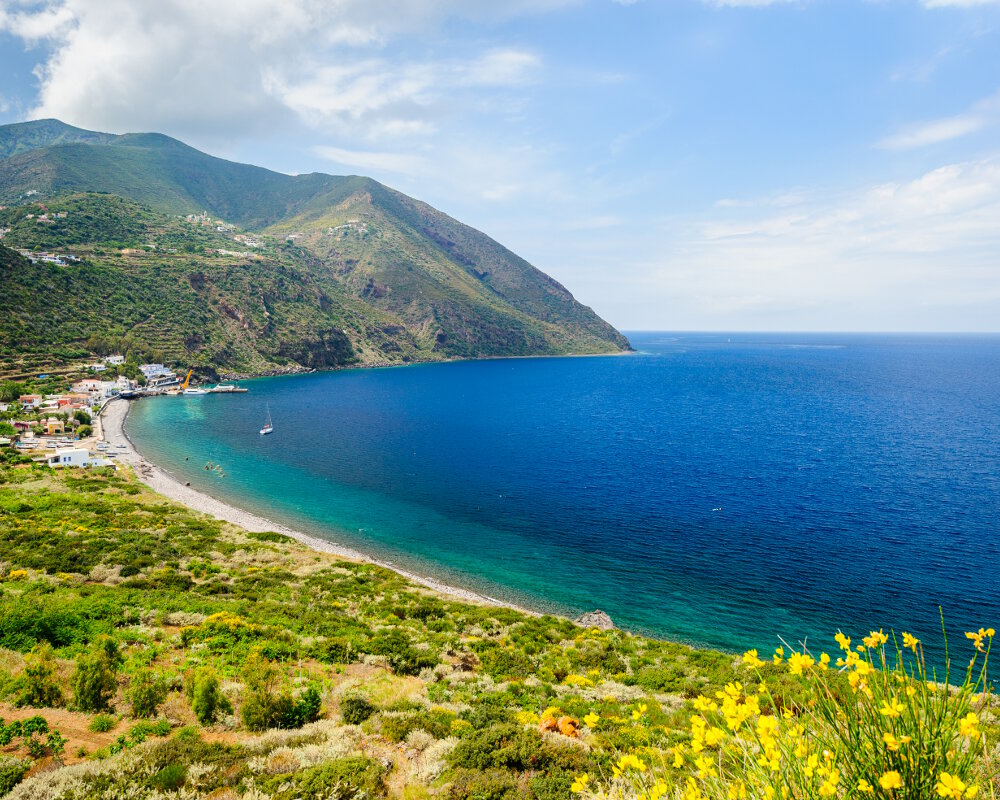 Une vue panoramique de la plage de galet del Porto avec au fond la jetée du port de Filicudi Une vue panoramique de la plage de galet del Porto avec au fond la jetée du port de Filicudi