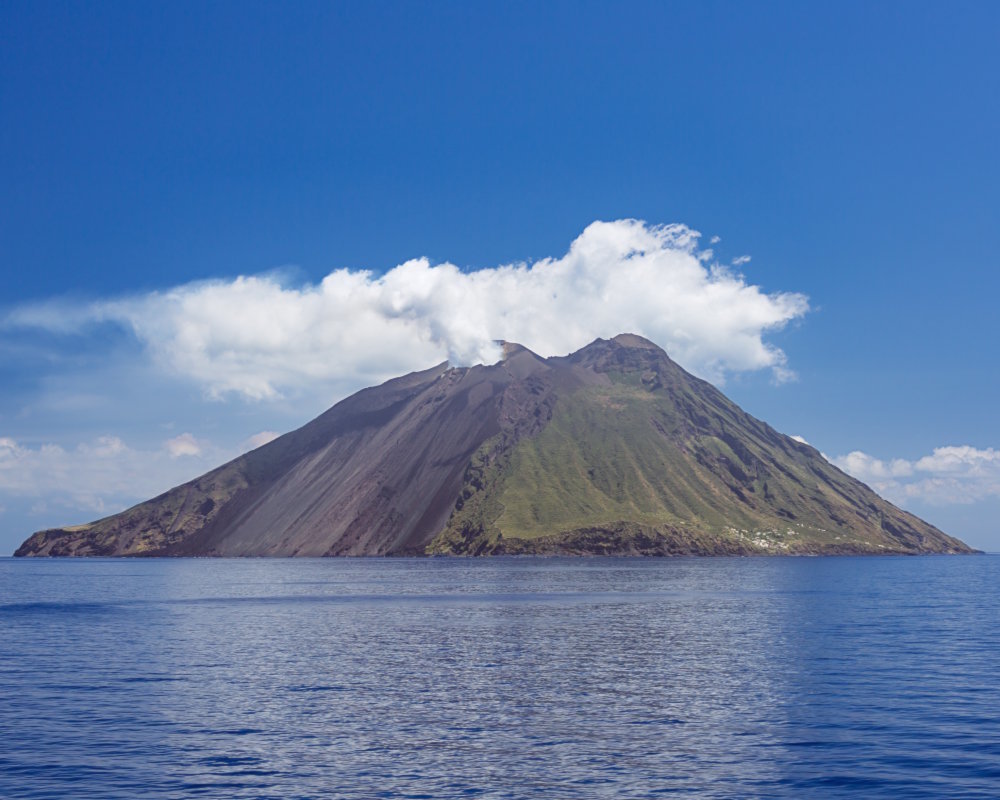 Stromboli island with its volcano topped by a plume of white fumaroles Stromboli island with its volcano topped by a plume of white fumaroles