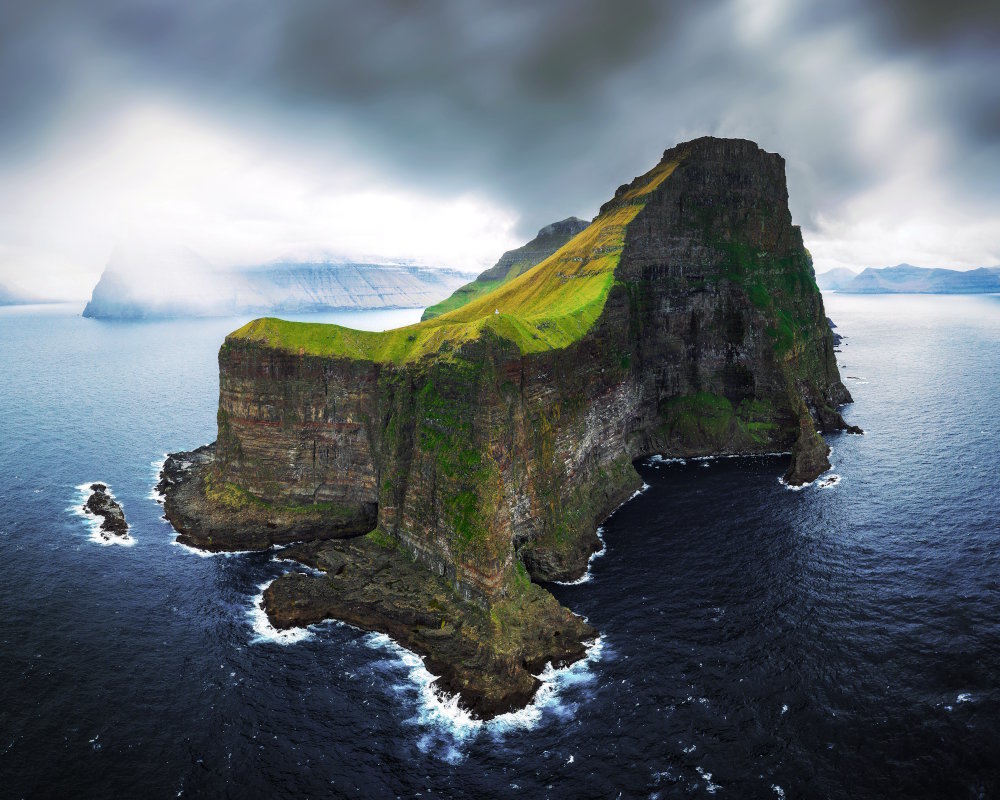 Aerial view of the dramatic cliffs of Kalsoy island in the Faroe islands, with the Kallur Lighthouse perched atop a cliff overlooking the Atlantic ocean